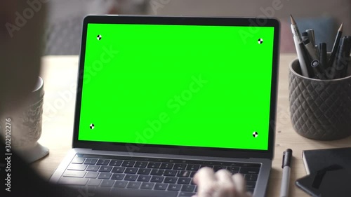 Over the shoulder shot of young woman working on modern laptop with green screen mock-up. Hands on keyboard.