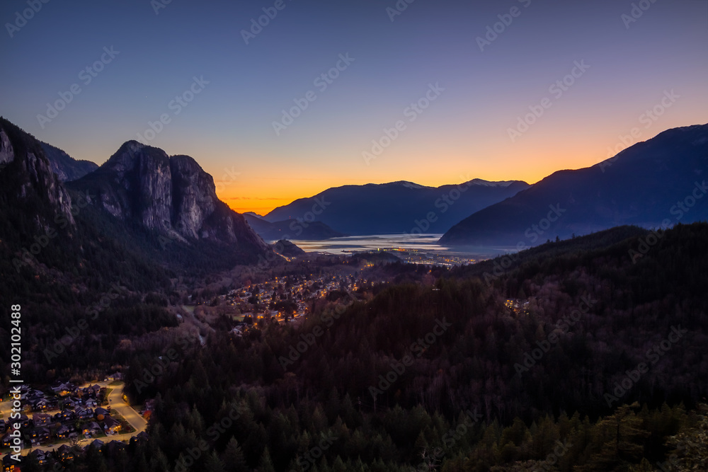 Squamish, North of Vancouver, British Columbia, Canada. Beautiful Aerial View from the top of the Mountain of a small town surrounded by Canadian Nature during Autumn Sunset.