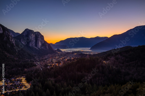 Squamish, North of Vancouver, British Columbia, Canada. Beautiful Aerial View from the top of the Mountain of a small town surrounded by Canadian Nature during Autumn Sunset.