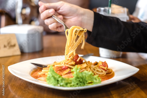 Close up of tasty Italian spaghetti taken up fron plate by woman hand using fork spoon. Woman eating Italian spaghetti at table in restaurant
