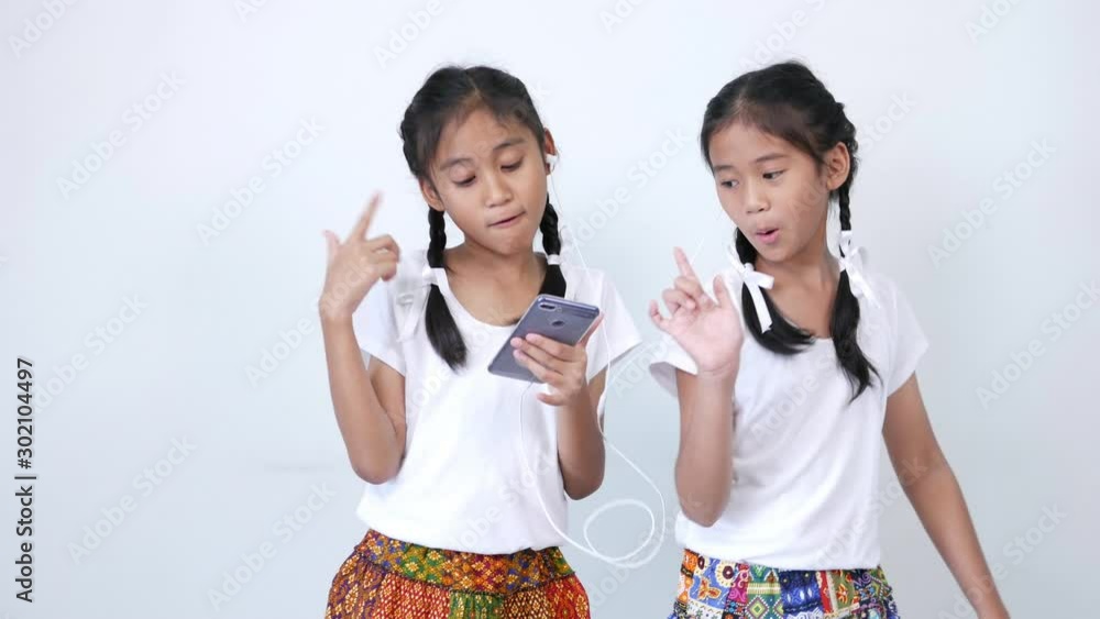 Two girl wore the white shirt, braid and tied lovely white ribbon, listening to music on smartphone with phone headset, enjoying and singing softly, follow the music and dance slowly. Two girl wore the white shirt, braid and tied lovely white ribbon, listening to music on smartphone with phone headset, enjoying and singing softly, follow the music and dance slowly.