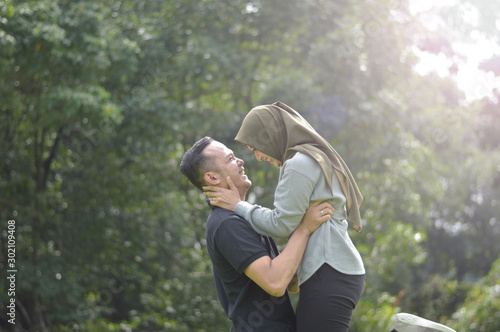 Outdoors photo, beautiful, young muslim couple, hugging and kissing and being affectionate with each other. nature in the background.