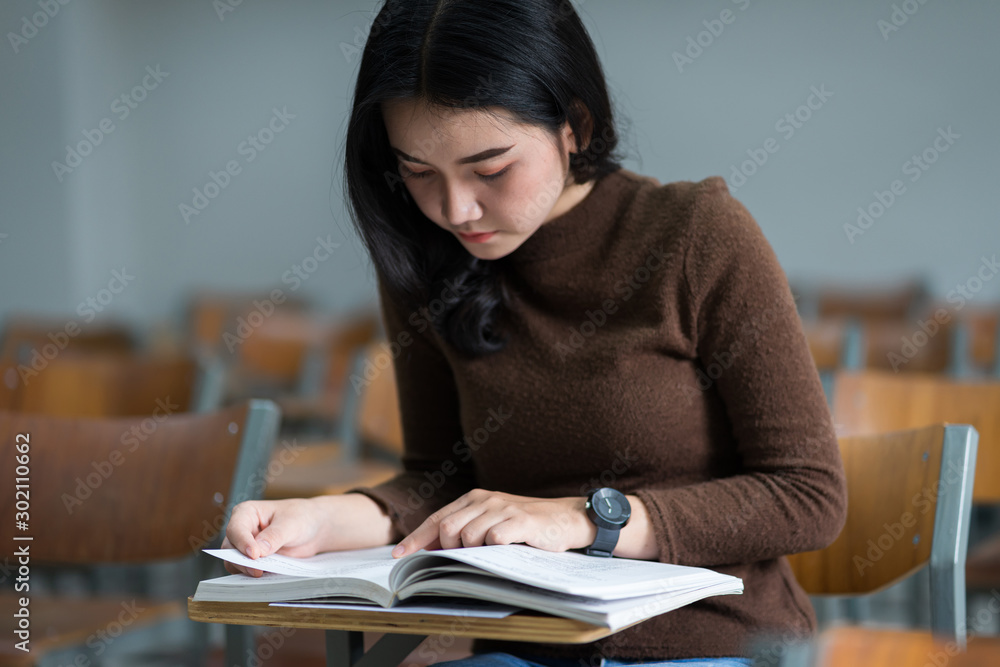 A teenager woman university student sits on wooden a chair concentrates reading textbook in the classroom preparing for examination. A teenager woman university student sits on wooden a chair concentrates reading textbook in the classroom preparing for examination.