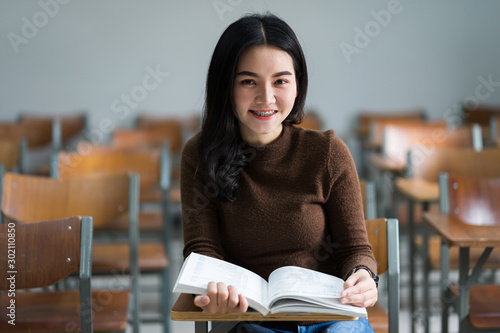 A teenager woman university student sits on wooden a chair concentrates reading textbook in the classroom preparing for examination.