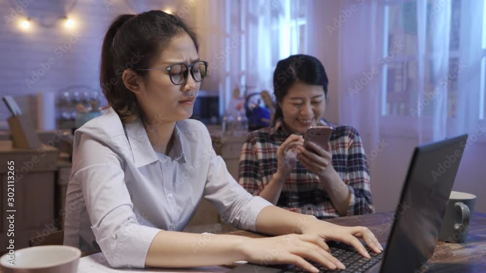 Angry worker scolding noisy roommate and telling to leave at kitchen table at home in night. business woman stay up late over work on notebook computer. annoying friend laughing use mobile phone Angry worker scolding noisy roommate and telling to leave at kitchen table at home in night. business woman stay up late over work on notebook computer. annoying friend laughing use mobile phone