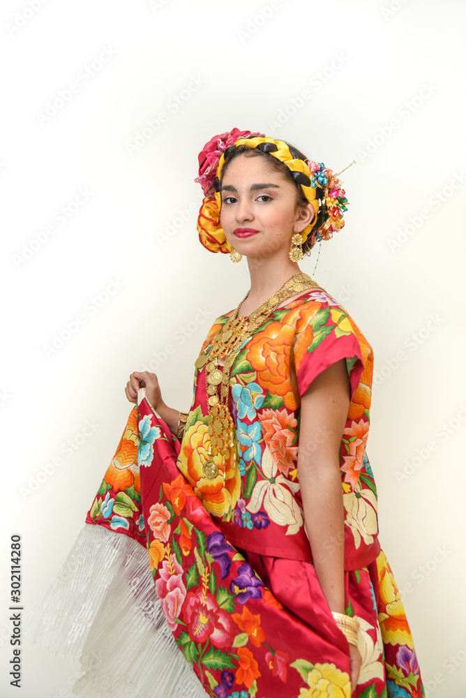 Mexican girl with a floral dress from Oaxaca Mexico, hidden in a red background with braided flowers and gold necklaces, for Mexican culture dance Mexican girl with a floral dress from Oaxaca Mexico, hidden in a red background with braided flowers and gold necklaces, for Mexican culture dance