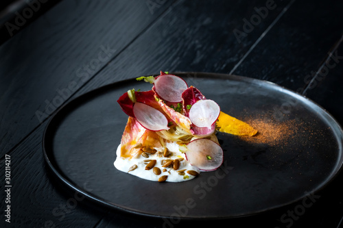 Haute cuisine salad with nuts, sauce and radish on a black dish at dark background