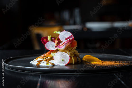 Haute cuisine salad with nuts, sauce and radish on a black dish at dark background photo