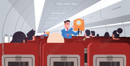 steward explaining for passengers how to use jacket life vest in emergency situation male flight attendants in uniform safety demonstration concept modern airplane board interior horizontal flat