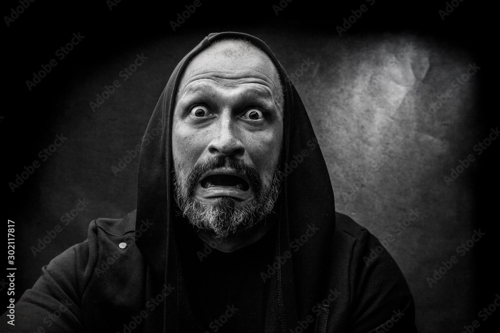 Black and white portrait of a bald bearded man in a hood on a dirty gray background