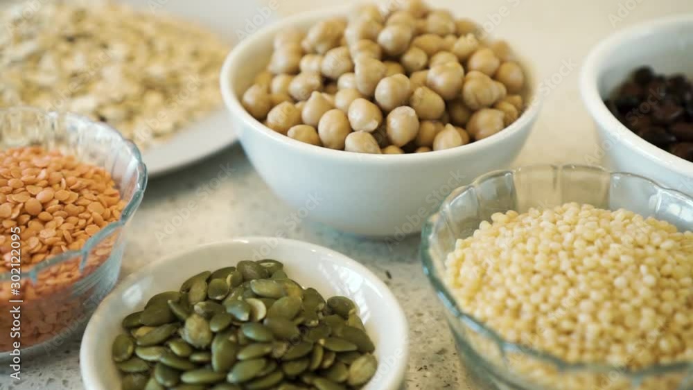 Various legumes, seeds and grains in bowls on white bench, pan close up Various legumes, seeds and grains in bowls on white bench, pan close up