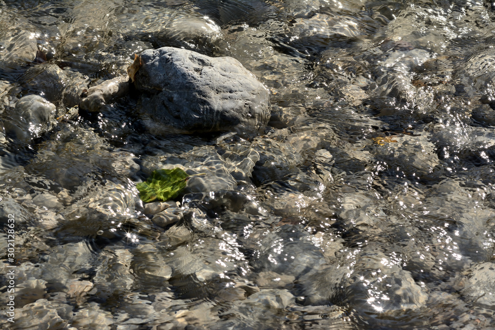 Stone, blurred pebbles and stones, a blurred green colored leaf underwater of a river in Provence. South of France.