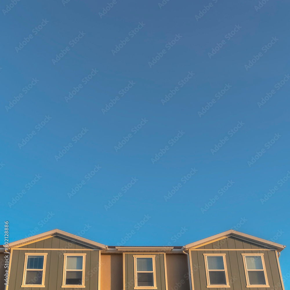 Square frame Upper storey of townhomes viewed from below against blue sky on a sunny day Square frame Upper storey of townhomes viewed from below against blue sky on a sunny day