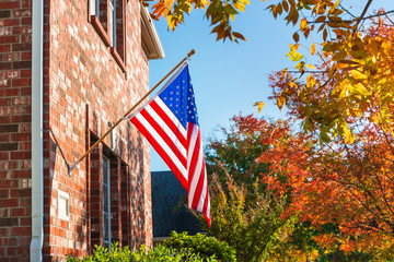 Patriotic American flag waving in front of a brick home on a sunny autumn day.