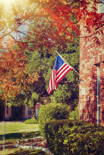 Patriotic American flag waving in front of a brick home on a sunny autumn day. Vintage filter effects.