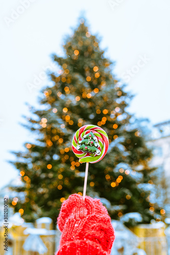 woman hand in red gloves holding candy in front of christmas tree