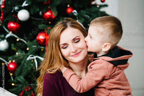 Son kiss mom near Christmas tree. Happy New Year and Merry Christmas. Christmas decorated interior. The concept of family holiday. Close up.