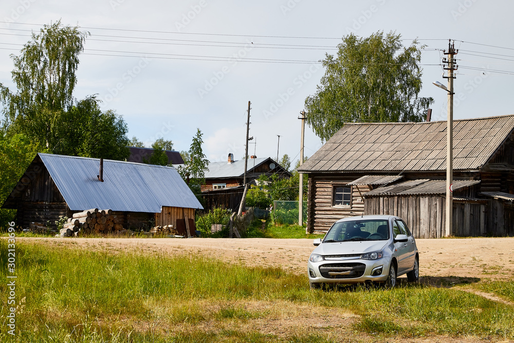 Car in a Russian village on the background of old wooden houses on a summer day