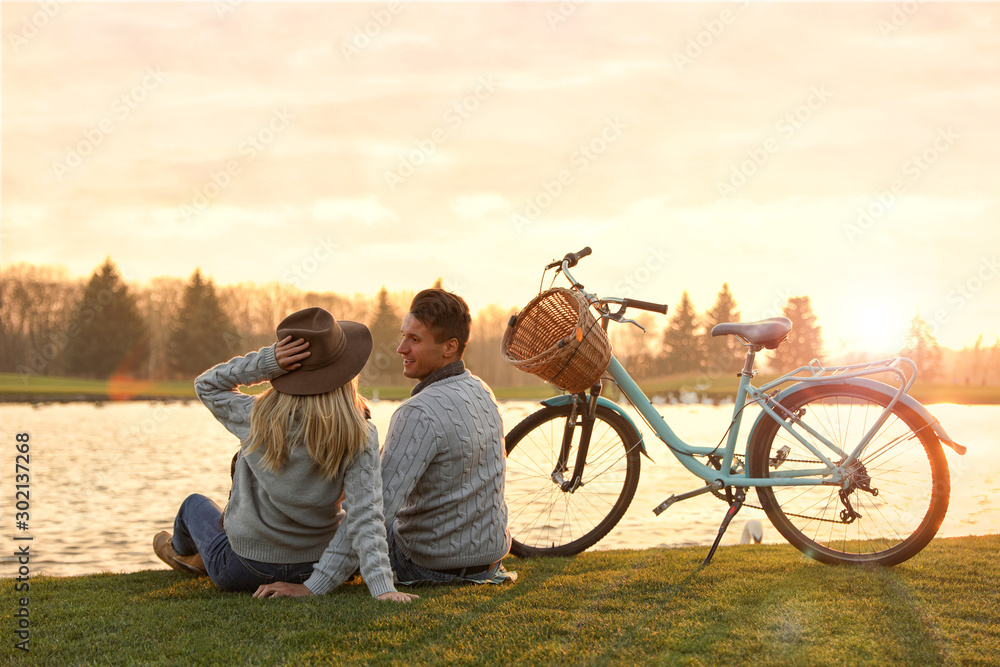 Young couple near lake at sunset. Perfect place for picnic - obrazy, fototapety, plakaty 