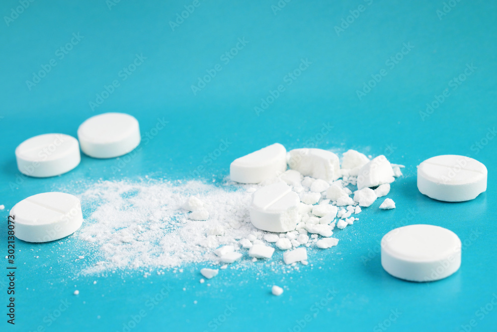 White pills on blue background. Two pills are crushed.  Selective focus - obrazy, fototapety, plakaty 
