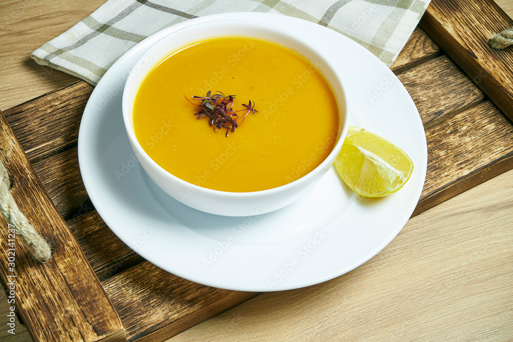 Lentil cream soup with a slice of lemon on a wooden tray in a white bowl. Healthy and vegan food. Go green. Close up Lentil cream soup with a slice of lemon on a wooden tray in a white bowl. Healthy and vegan food. Go green. Close up