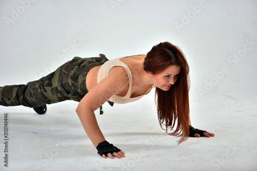 Fototapeta Naklejka Na Ścianę i Meble -  girl with red hair in a military uniform and black gloves does sports military exercises