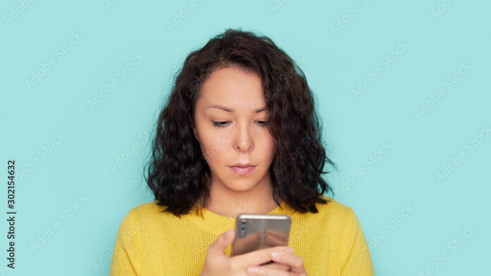 woman using smartphone over blue background. Wearing in in a yellow knitted sweater woman using smartphone over blue background. Wearing in in a yellow knitted sweater