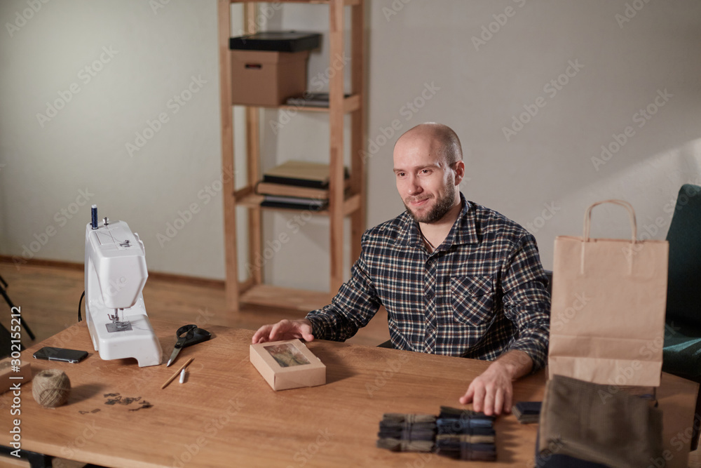 Man packs wool bow tie in box. Young man working as a tailor and using a sewing machine in workshop. Man packs wool bow tie in box. Young man working as a tailor and using a sewing machine in workshop.
