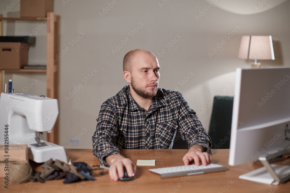 Man on the computer makes out the delivery of the online store. Working with sewing machine in a textile studio. Tailor makes bow ties of woolen fabric. Man on the computer makes out the delivery of the online store. Working with sewing machine in a textile studio. Tailor makes bow ties of woolen fabric.