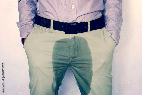 A man standing in wet pants against the wall. Urinary incontinence is an increasingly popular disease affecting younger males. incontinence and wet pants. a dark spot on a light trousers. photo