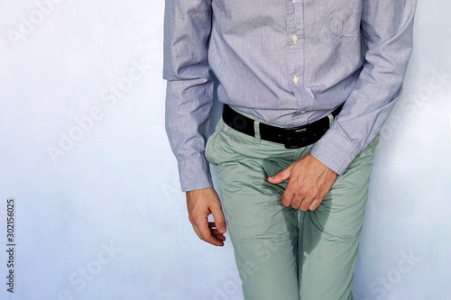 Fotografie Close up of a man with hands holding his crotch on a light blue background