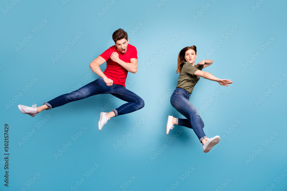 Full size photo of two people crazy funky successful married ninja couple jump practice martial fighting exercises wear green red t-shirt modern outfit isolated over blue color background