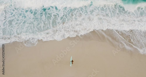 Aerial view of a woman on the beach going surfing