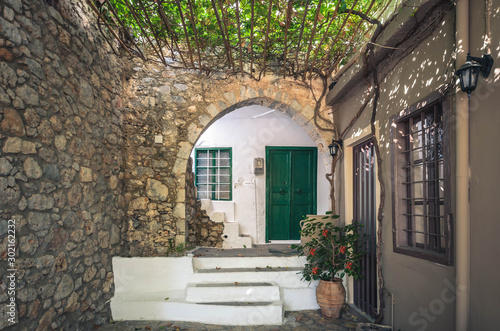 Typical greek courtyard with wooden door  stone arch  grapevine and stairs painted in white  in a traditional village of Crete.