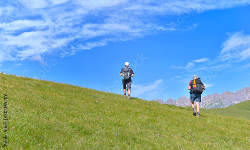 hikers climbing a grassy hill in alpine mountain under blue sky