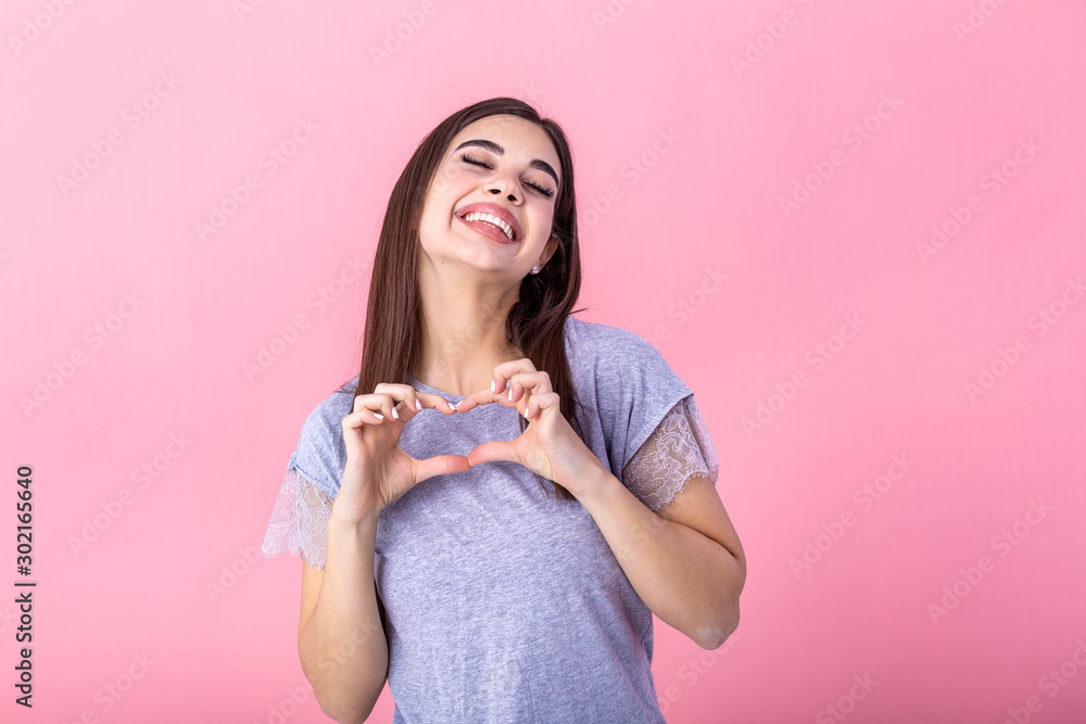 Portrait of a smiling young beautiful woman showing heart gesture with two hands and looking at camera isolated over pink background Portrait of a smiling young beautiful woman showing heart gesture with two hands and looking at camera isolated over pink background