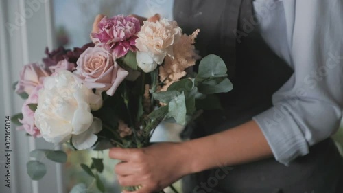 Close up of female florist's hands arranging iris, peopnies, hydrangea flowers, eucalyptus for bouquet in the flower shop, side view