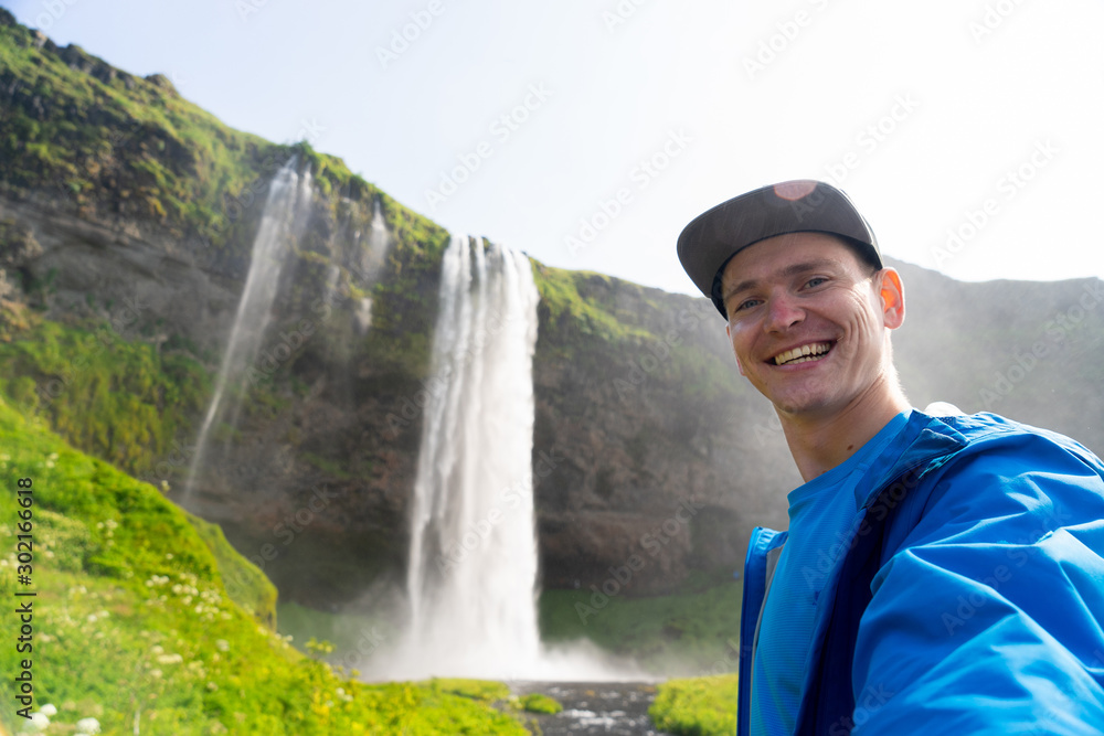 Young man taking selfie with beautiful waterfall of Seljalandsfoss on background. Concept of traveling and healthy lifestyle
