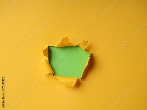 Small paper hole with torn sides over yellow background for your text, print or promotional content. Through paper. Ripped hole. No people. Accurate shot. Advertising and breakthrough concept