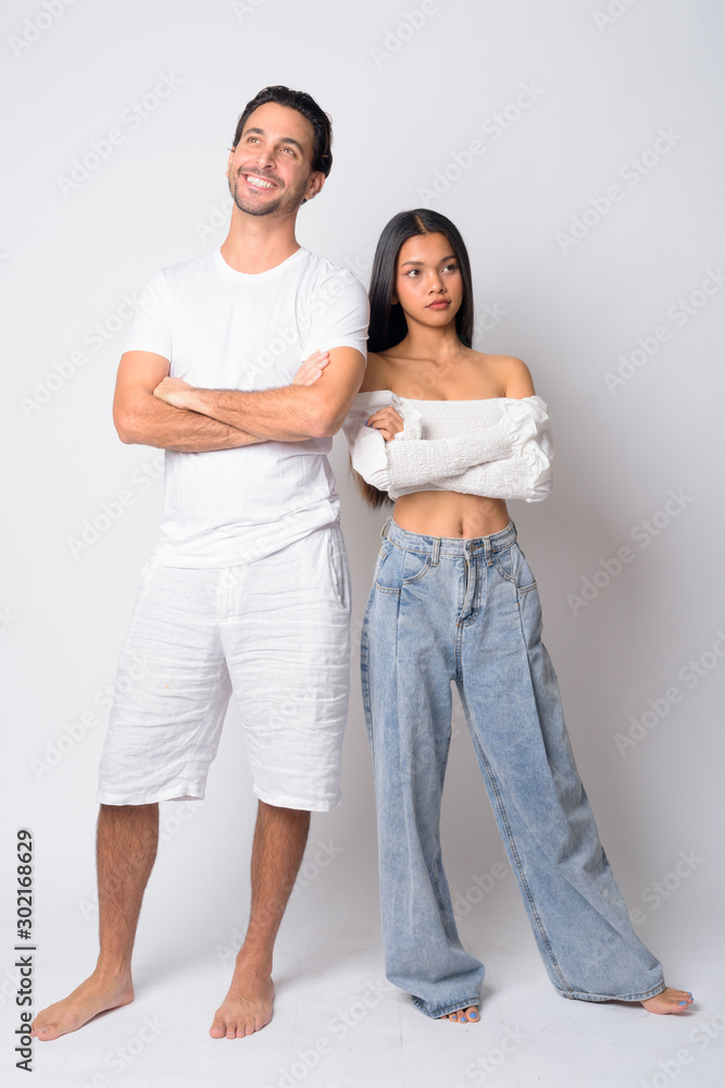Full body shot of happy multi ethnic couple thinking together with arms crossed Full body shot of happy multi ethnic couple thinking together with arms crossed