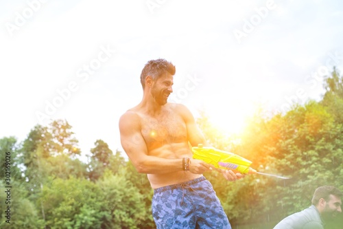 Shot of cheerful man enjoying with squirt guns on pier during summer