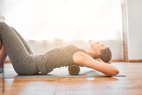 Woman doing yoga lying on massager on rug in gym photo