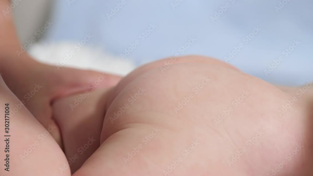 Mom wipes baby's buttocks with wet wipe. Child lies on white blanket on blue background, mother wipes his buttocks with wet cloth. Slow motion Mom wipes baby's buttocks with wet wipe. Child lies on white blanket on blue background, mother wipes his buttocks with wet cloth. Slow motion