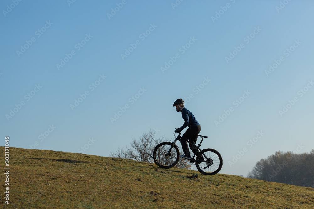 Cyclist in pants and fleece jacket on a modern carbon hardtail bike with an air suspension fork rides off-road.