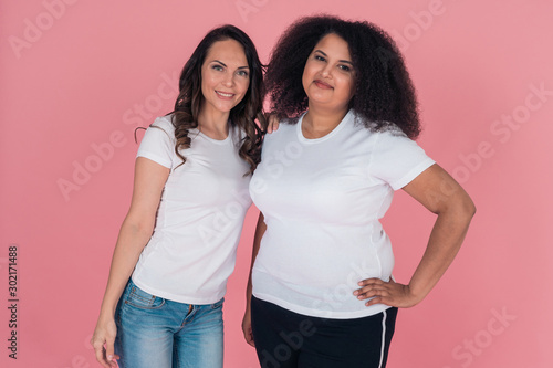 Two cute girls an African American and a Caucasian girl smile directly at the camera in white t shirts on a pink background