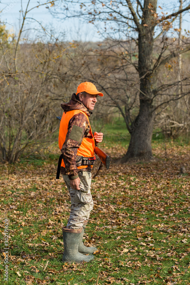 Hunting period, autumn season open. A hunter with a gun in his hands in hunting clothes in the autumn forest in search of a trophy. A man stands with weapons and hunting dogs tracking down the game. Hunting period, autumn season open. A hunter with a gun in his hands in hunting clothes in the autumn forest in search of a trophy. A man stands with weapons and hunting dogs tracking down the game.