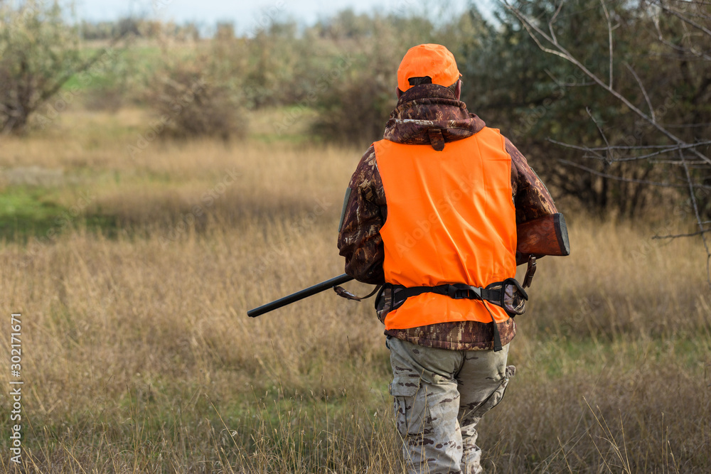 Hunting period, autumn season open. A hunter with a gun in his hands in hunting clothes in the autumn forest in search of a trophy. A man stands with weapons and hunting dogs tracking down the game.	
