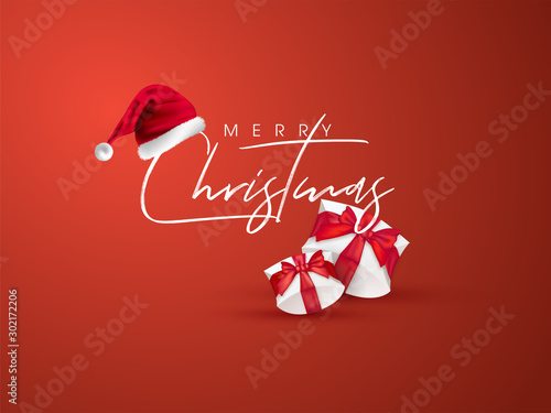 Calligraphy text Merry Christmas with santa hat and gift boxes on orange background can be used as greeting card design.