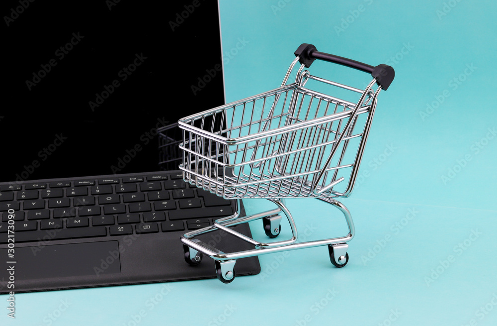 Internet shopping concept of a laptop computer with a mini shopping cart basket resting on the keyboard isolated against an green background
