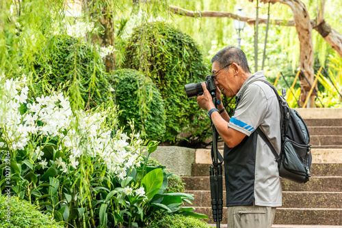 Active Asian Chinese senior male man taking photographs with his digital DSLR camera
